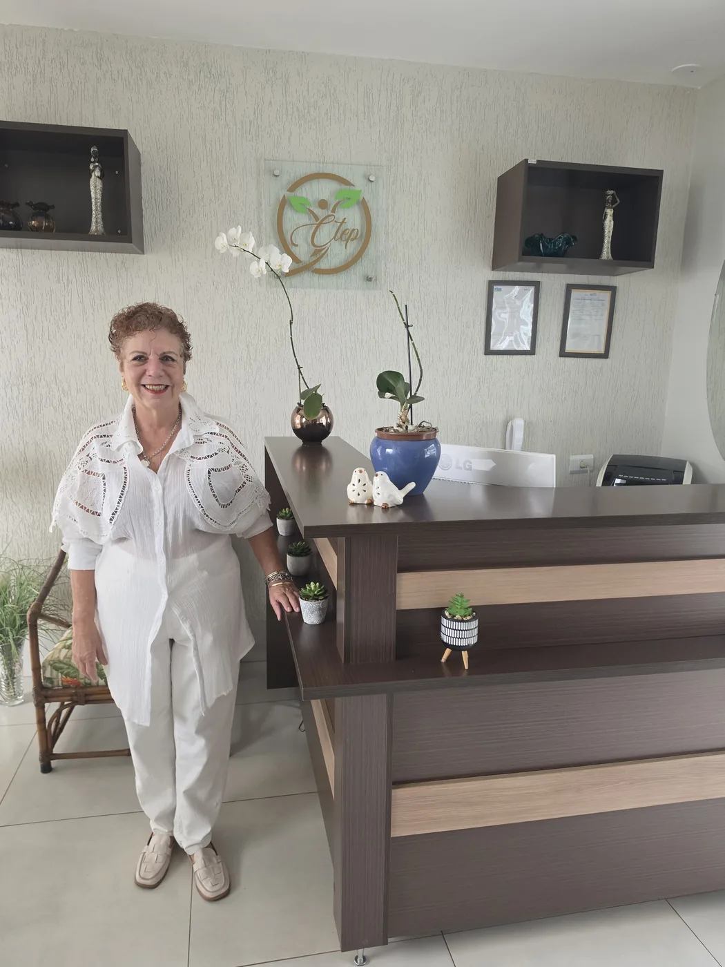 Beth Perez na recepção do CTEP ao lado do logotipo do centro