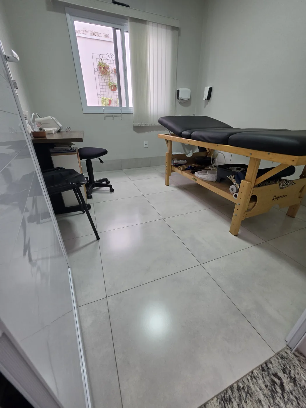 Sala de atendimento com maca de tratamento e mesa de apoio