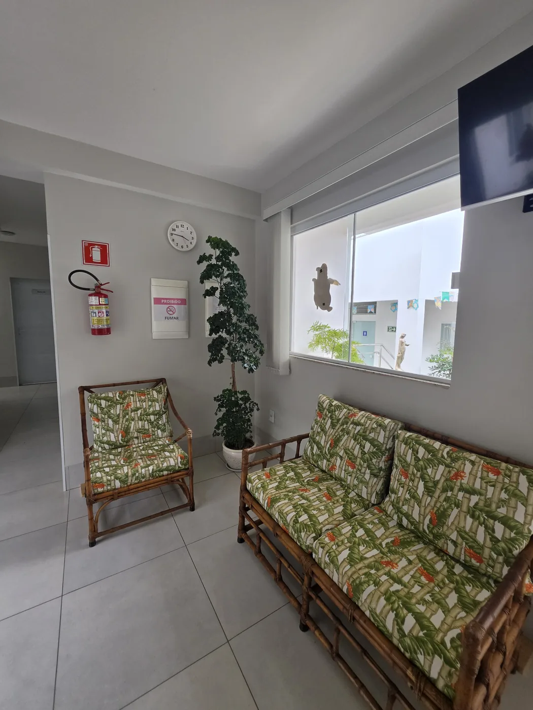 Sala de espera com sofás de fibra natural e estampa de folhagens